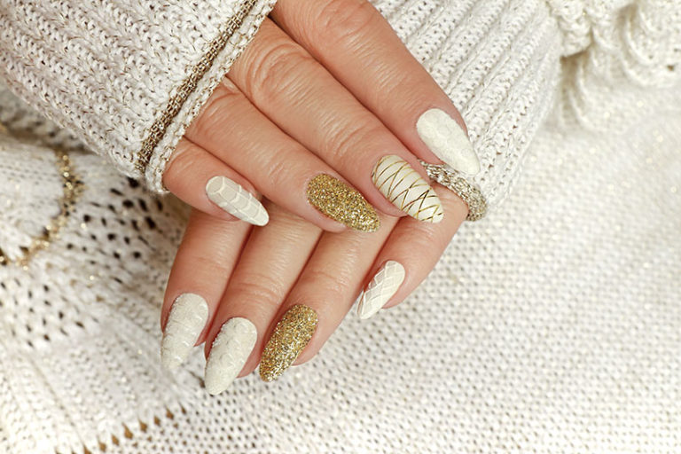 Knitted sand manicure on long oval nails with golden sequins and threads on a woman's hand in a jacket. Winter trend in nail design.